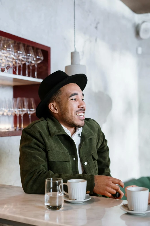 two men sitting at a table with cups of coffee, a portrait, inspired by Barthélemy Menn, trending on unsplash, he is wearing a hat, robert sheehan, proud looking, wearing a fancy jacket