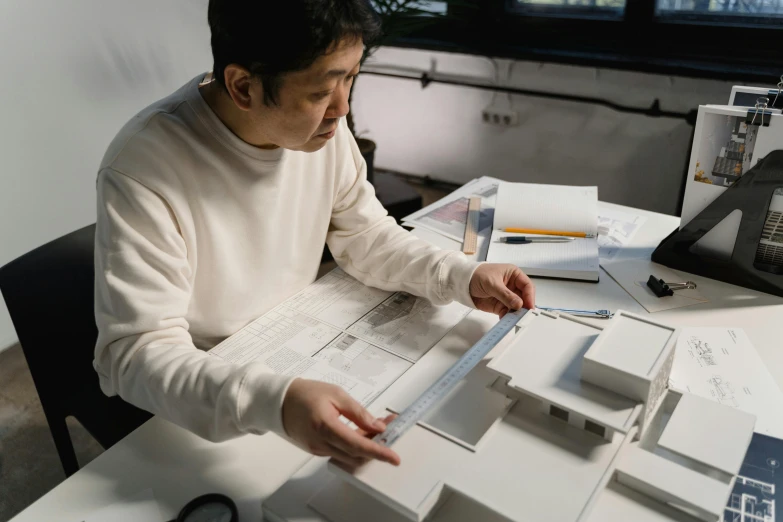 a man sitting at a table working on a model, inspired by Takeuchi Seihō, pexels contest winner, dezeen showroom, mei-ling zhou, creating a soft, panels