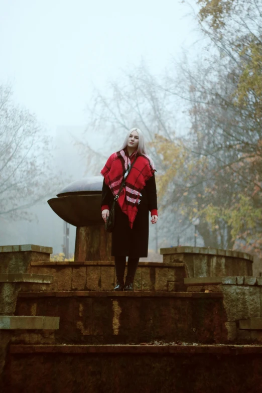 a woman standing in front of a fountain on a foggy day, an album cover, red scarf, in a graveyard, grunge rock, bridges