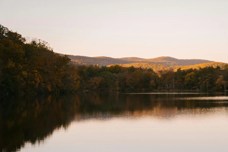 a large body of water surrounded by trees, by Carey Morris, trending on unsplash, hudson river school, autumn sunrise warm light, medium format. soft light, ignant, hills in the background