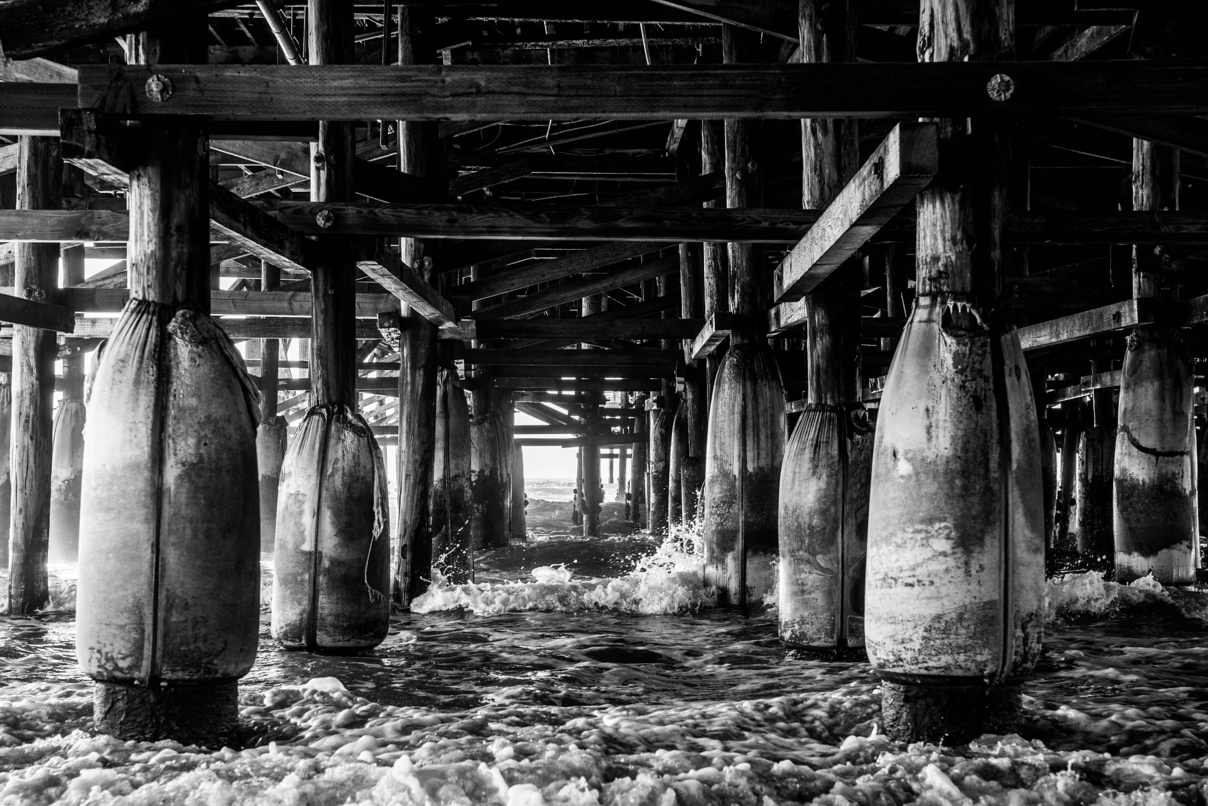 a black and white photo of the inside of a pier, by David Palumbo, process art, bottles, large pillars, covered in ice, oceanside