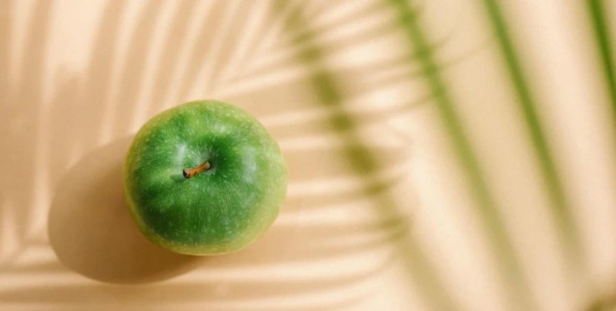 a green apple sitting on top of a table, by Emma Andijewska, trending on pexels, tropical style, phong shaded, oiled skin, miniature product photo