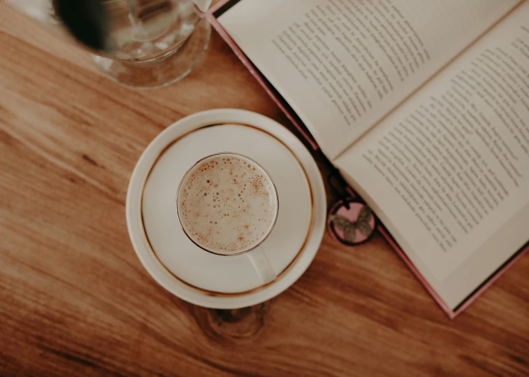 an open book sitting on top of a wooden table next to a cup of coffee, a portrait, pexels contest winner, private press, cappuccino, round-cropped, background image, jenna barton