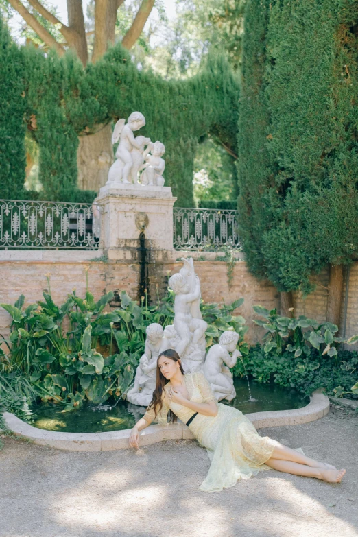 a woman laying on the ground in front of a fountain, a statue, inspired by Oleg Oprisco, unsplash, rococo, :: madison beer, in a verdant garden, lady of elche, delightful surroundings