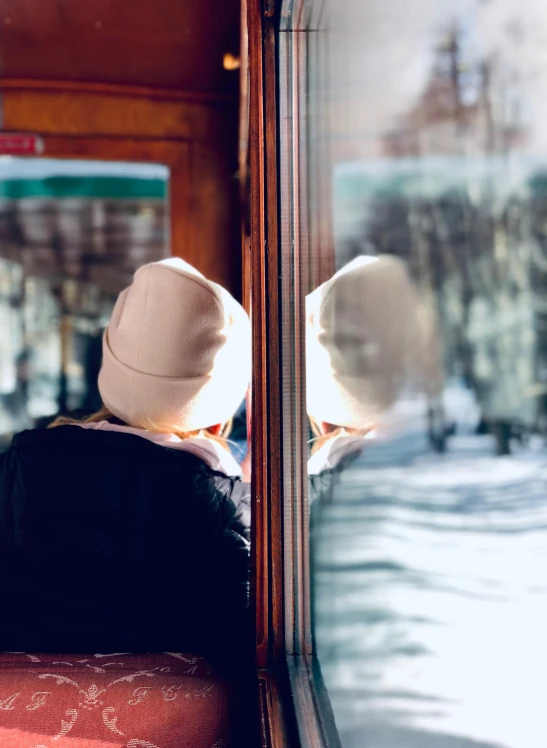 two people sitting on a train looking out the window, by Julia Pishtar, pexels contest winner, symbolism, cold snow outside, hat covering eyes, view from behind mirror, profile image