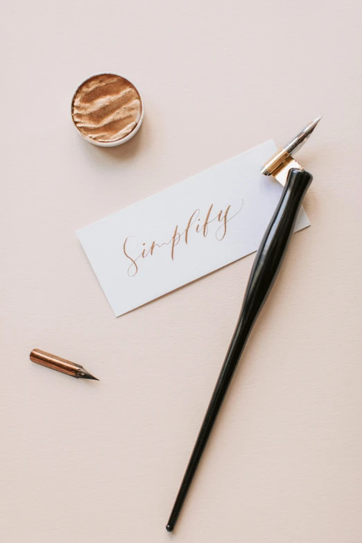 a pen and a note sitting on top of a table, a still life, by Sam Charles, trending on unsplash, graceful beauty, on a pale background, gold and silver ink, letter s