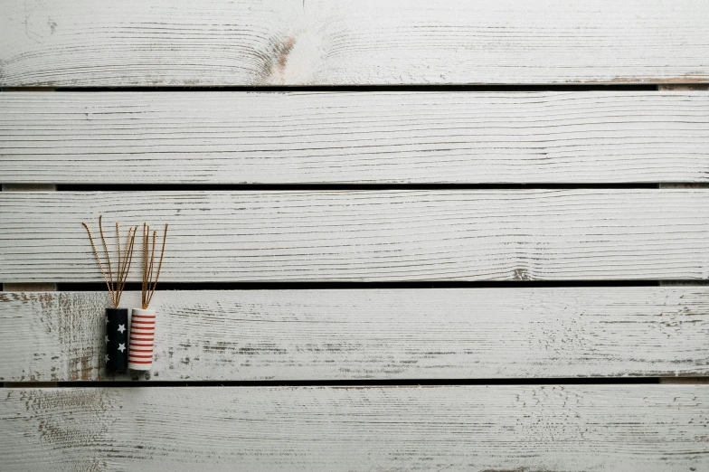 a couple of sticks sitting on top of a wooden table, inspired by Okada Hanko, unsplash, minimalism, fireworks, white plank siding, white red, striped