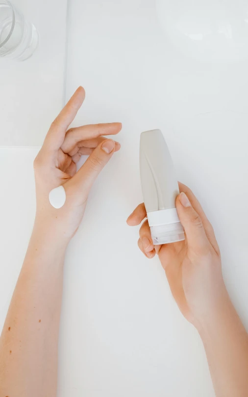 a person holding a tube of lotion next to a bottle of lotion, by Nicolette Macnamara, unsplash, light grey mist, issey miyake, white background : 3, light emitting from fingertips