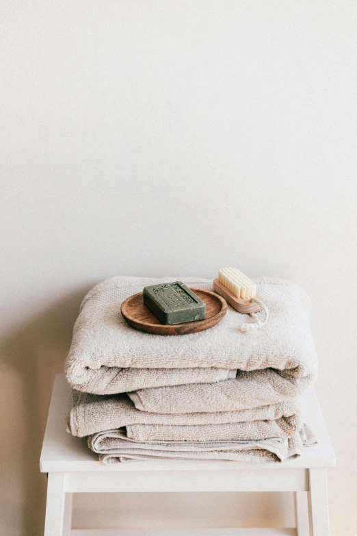 a stack of towels sitting on top of a white stool, trending on unsplash, carved soap, dark green, full-body, on a wooden tray