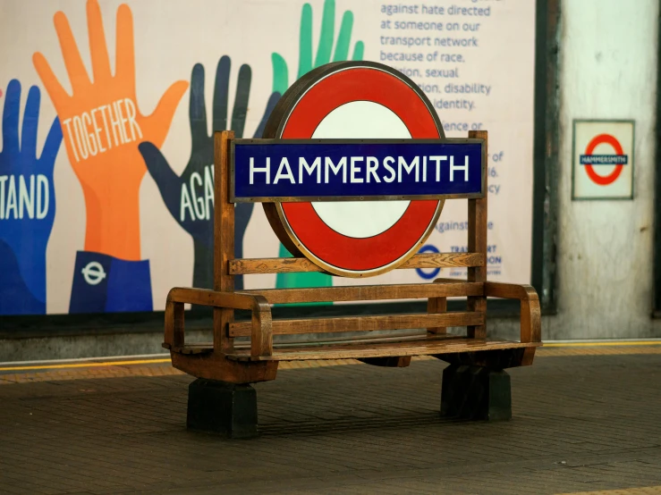 a wooden bench sitting in front of a sign, an album cover, inspired by Ian Hamilton Finlay, unsplash, mannerism, london underground tube station, hammer's slammers, male holosmith, hands raised