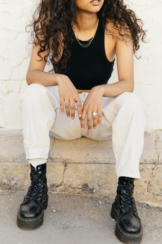 a woman sitting on the steps of a building, inspired by L. A. Ring, trending on pexels, renaissance, white pants, gnarled fingers, rugged black clothes, curly haired