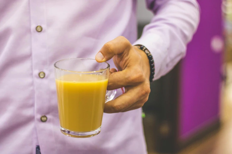 a man holding a glass of orange juice, pexels, yellow and purple color scheme, is ((drinking a cup of tea)), cream of the crop, moringa juice