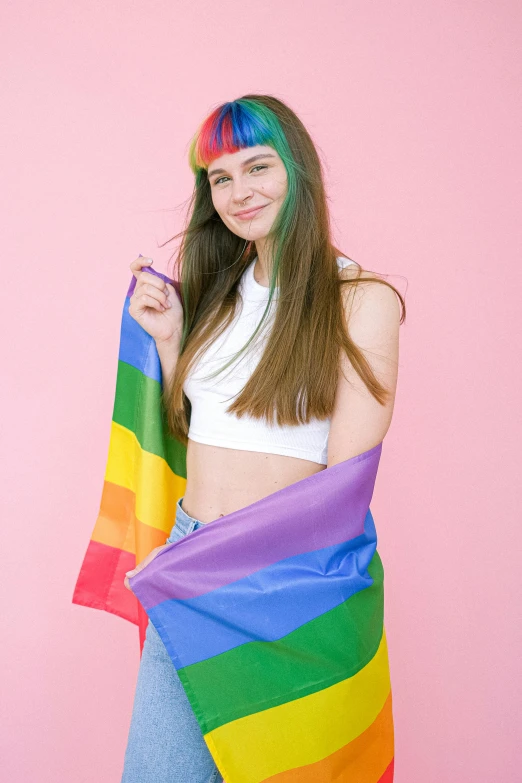 a woman standing in front of a pink wall holding a rainbow flag, an album cover, by Julia Pishtar, trending on pexels, brown colored long hair, bandanas, teenage boy, 🍸🍋