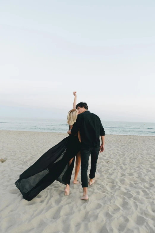 a man and woman standing on top of a sandy beach, unsplash, romanticism, in a black chiffon layered robe, back, denim, flowy