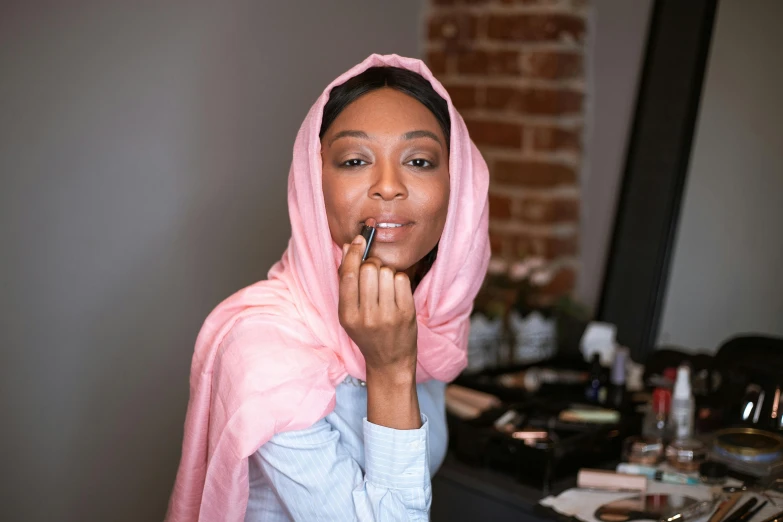 a woman putting on lipstick in front of a mirror, inspired by Charly Amani, featured on instagram, wearing a veil, brown skin. light makeup, mecca, ready to model