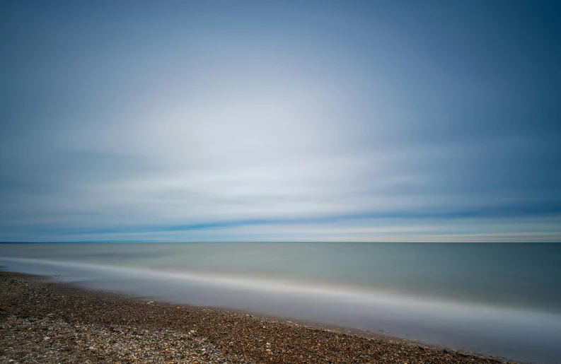 a large body of water sitting on top of a sandy beach, by Andrew Bell, minimalism, long exposure photo, uniform plain sky, multicoloured, blue gray