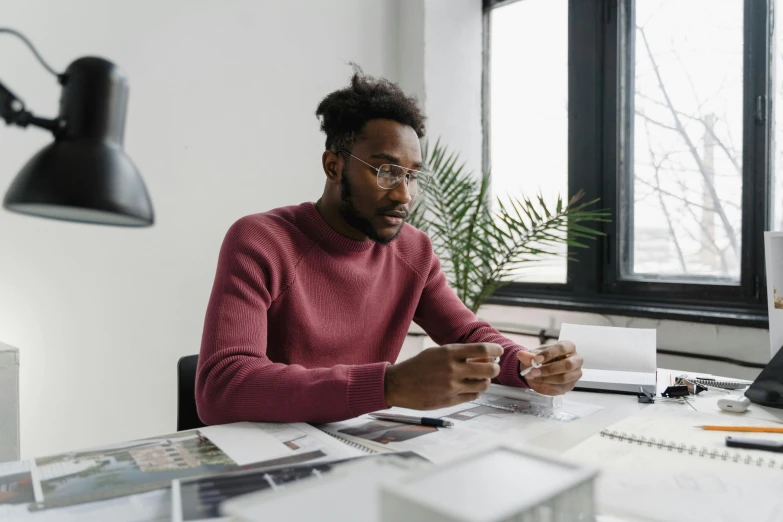 a man sitting at a desk in front of a computer, inspired by Afewerk Tekle, pexels contest winner, looking at his phone, he is wearing a brown sweater, architect, on a white table