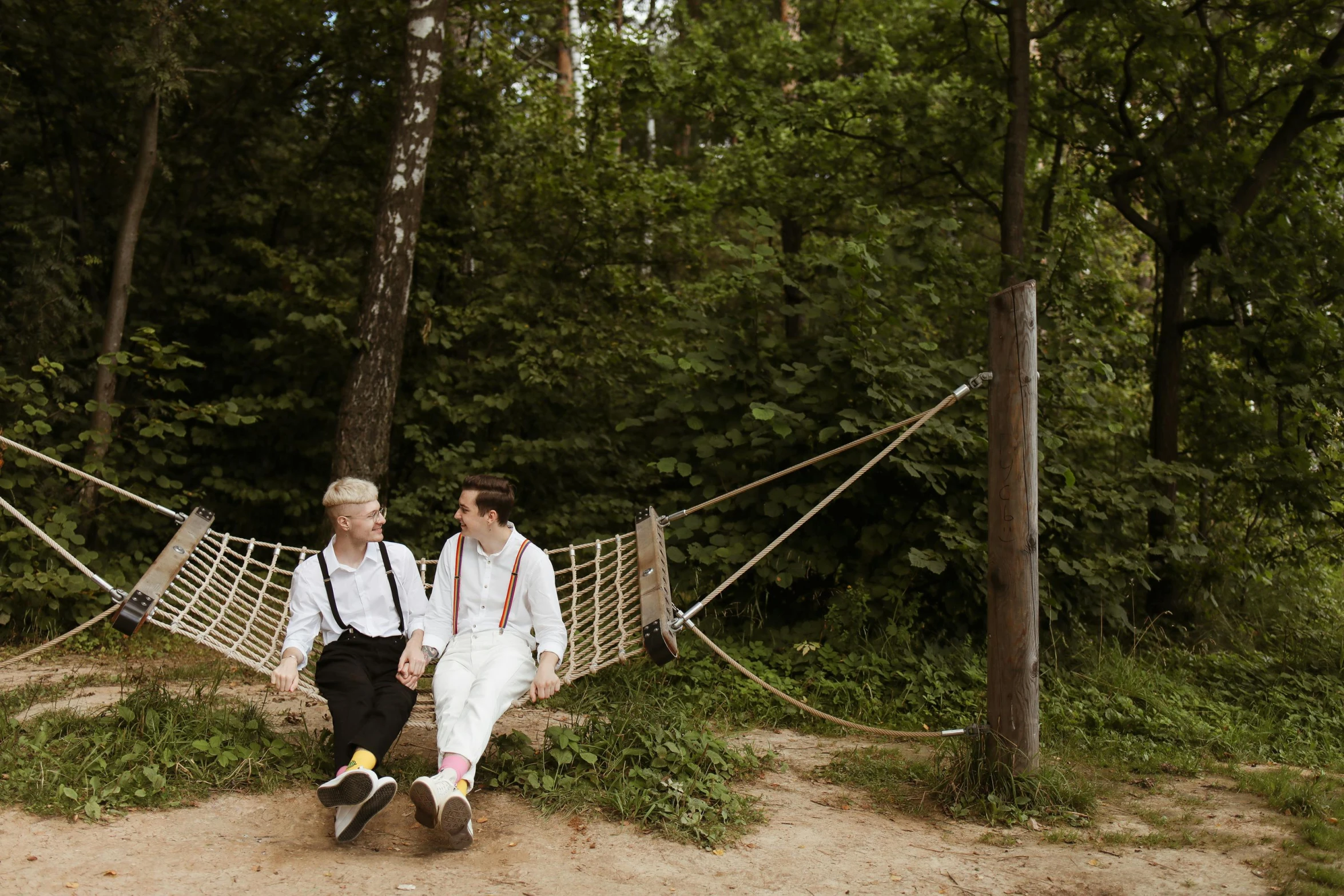 a couple of men sitting on top of a hammock, by Emma Andijewska, romanticism, midsommar style, political meeting in the woods, conde nast traveler photo, non-binary