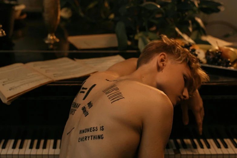 a man sitting at a piano with a tattoo on his back, trending on pexels, julia garner, androgynous, devastated, thumbnail