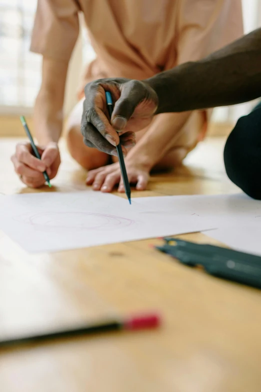 a person sitting on the floor drawing on a piece of paper, by Jessie Algie, pexels contest winner, beautiful people, collaboration, kai carpenter, split near the left