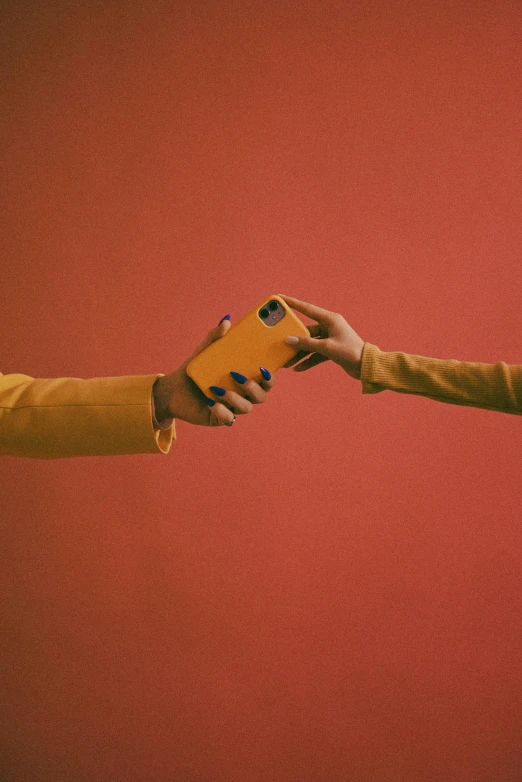 two people shaking hands in front of a red wall, an album cover, trending on pexels, aestheticism, holding a very advance phone, yellow and ornage color scheme, toy camera, her friend