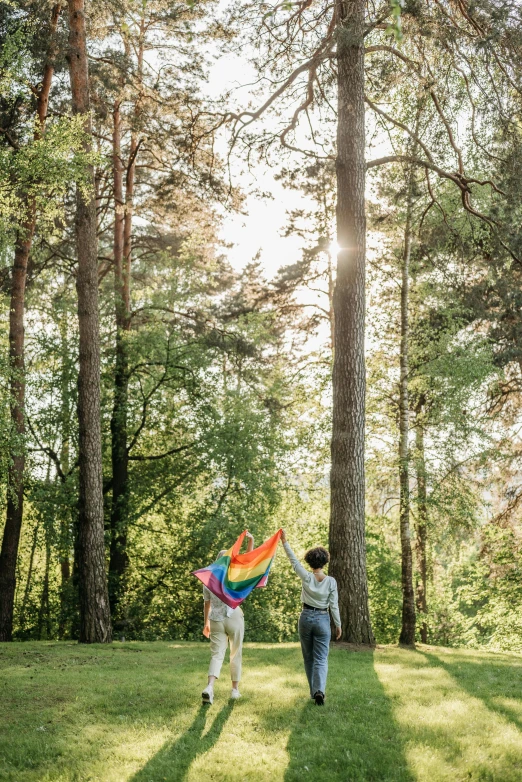 a couple of people that are standing in the grass, by Okuda Gensō, pexels contest winner, walking through the trees, lesbian, forest picnic, flag in hands up