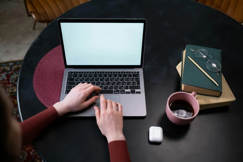 a woman sitting at a table using a laptop computer, by Carey Morris, trending on pexels, top-down shot, table in front with a cup, thumbnail, round format