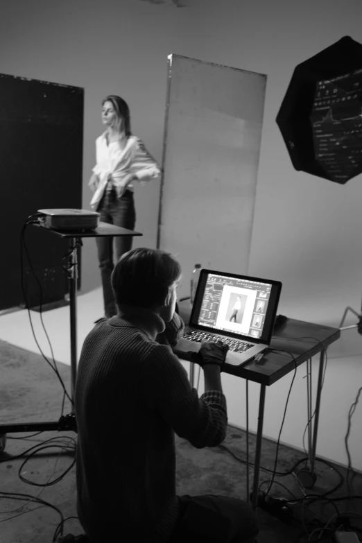 a man sitting in front of a laptop computer, a black and white photo, by Clifford Ross, instagram, photorealism, on a mannequin. studio lighting, girl in studio, two models in the frame, behind the scenes photography