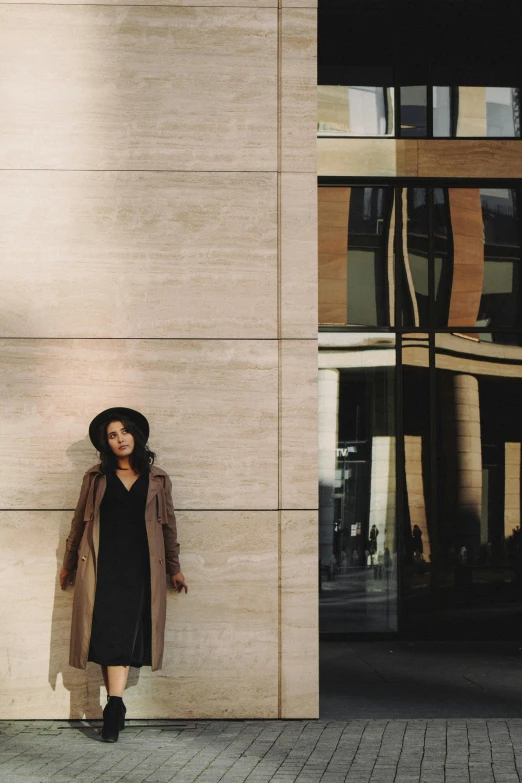 a woman standing in front of a tall building, pexels contest winner, straw hat and overcoat, black and brown colors, instagram picture, modern earthy neutral earthy