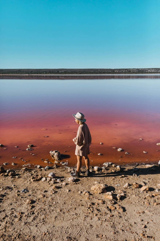 a person standing in front of a body of water, inspired by Scarlett Hooft Graafland, process art, earthy colours, red river, manuka, shades of pink