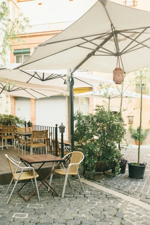 a patio with tables and chairs under an umbrella, a portrait, by Hirosada II, unsplash, madrid, yard, soft shade, gif