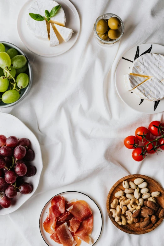 a white table topped with plates of food, a still life, trending on pexels, grapes, background image, silk, flat lay