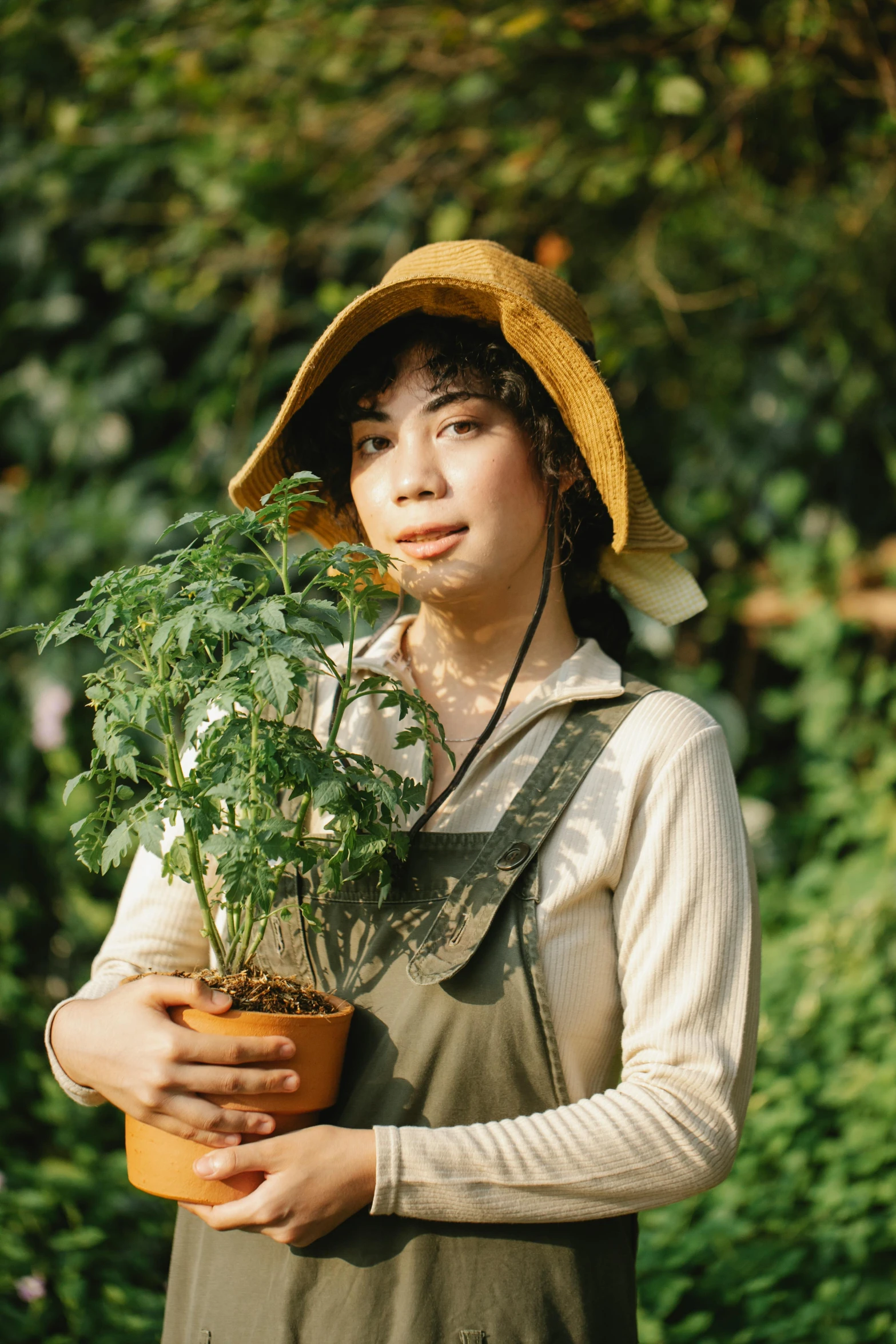 a woman holding a potted plant in a garden, inspired by Ruth Jên, unsplash, renaissance, wearing farm clothes, finn wolfhard, indonesia, portrait image