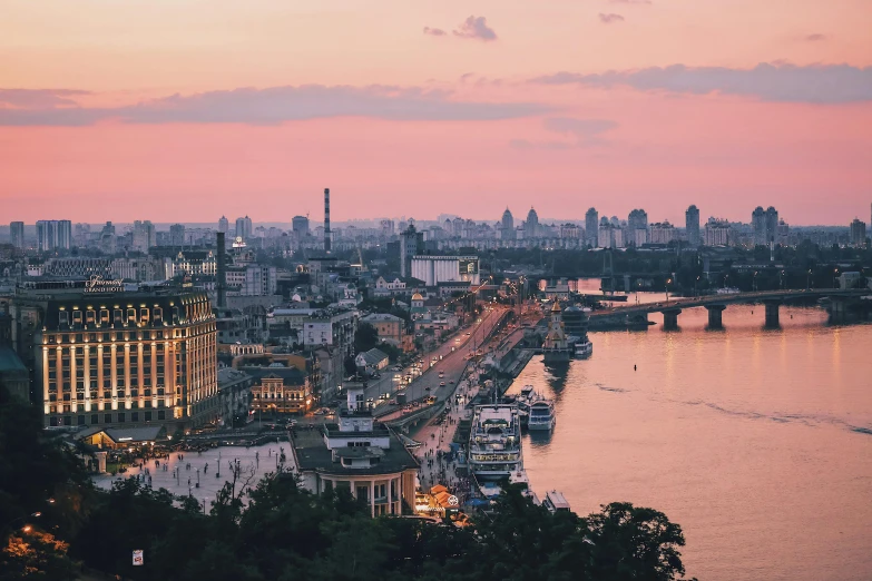 a view of a city from the top of a hill, by Emma Andijewska, pexels contest winner, ukrainian flag on the left side, great river, at dusk, with stalinist style highrise