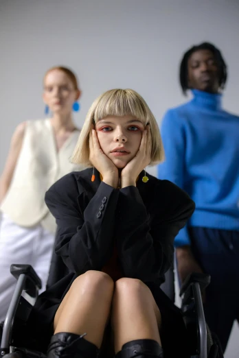 a woman sitting in a wheel chair in front of a group of people, inspired by Vanessa Beecroft, trending on pexels, frown fashion model, dressed anya taylor - joy, girl in studio, coloured