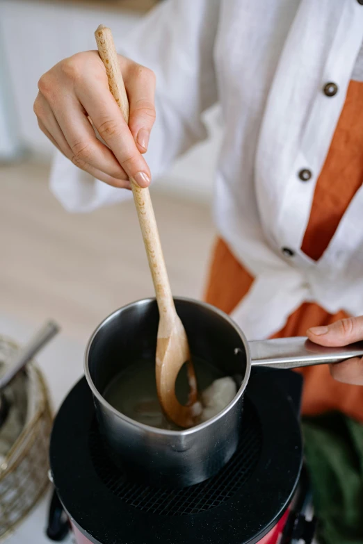 a woman stirring a pot of soup with a wooden spoon, inspired by Inshō Dōmoto, unsplash, square, low detail, cream, chemistry
