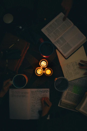 a group of people sitting around a table with books and candles, by Jessie Algie, pexels contest winner, moody hazy lighting, religious, wide overhead shot, 15081959 21121991 01012000 4k
