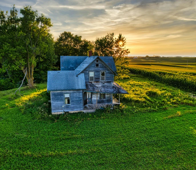 an old wooden house sitting on top of a lush green field, inspired by Gregory Crewdson, unsplash contest winner, sun down golden hour, drone view, iowa, “derelict architecture buildings