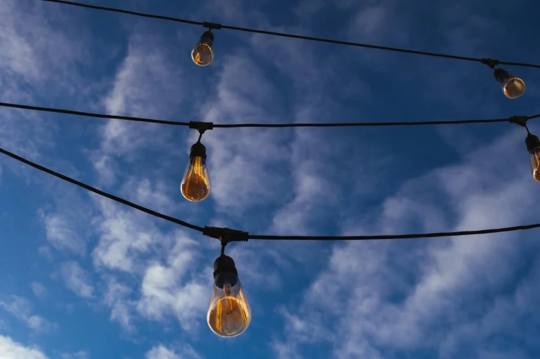 a bunch of light bulbs hanging from a wire, unsplash, blue skies, golden dapple lighting, in a row, brown