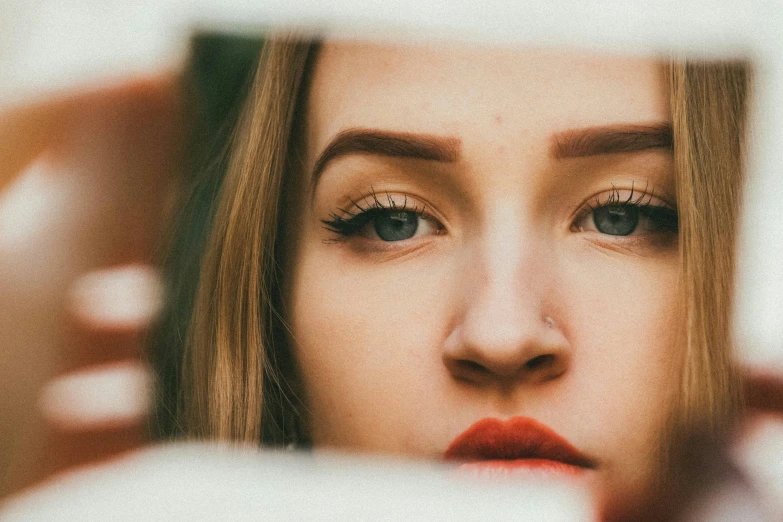 a woman looking at her reflection in a mirror, inspired by Elsa Bleda, trending on pexels, photorealism, square face, portrait of kim petras, small eyebrows, human face with bright red yes