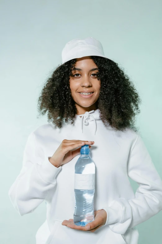 a woman in a white hoodie holding a bottle of water, pexels contest winner, renaissance, baggy clothing and hat, long afro hair, wearing a school uniform, plain background