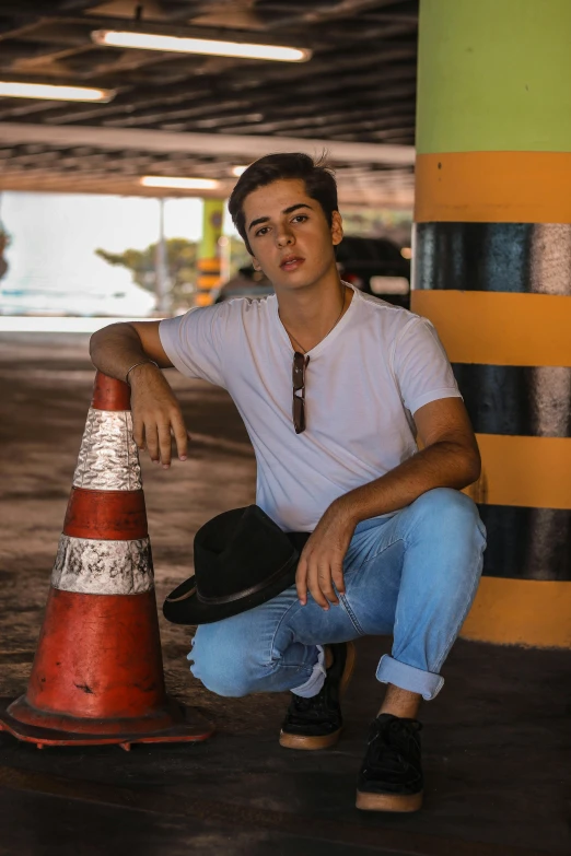 a man squatting next to a traffic cone, an album cover, by Robbie Trevino, pexels contest winner, handsome young man, caracter with brown hat, brazilan supermodel, young teen
