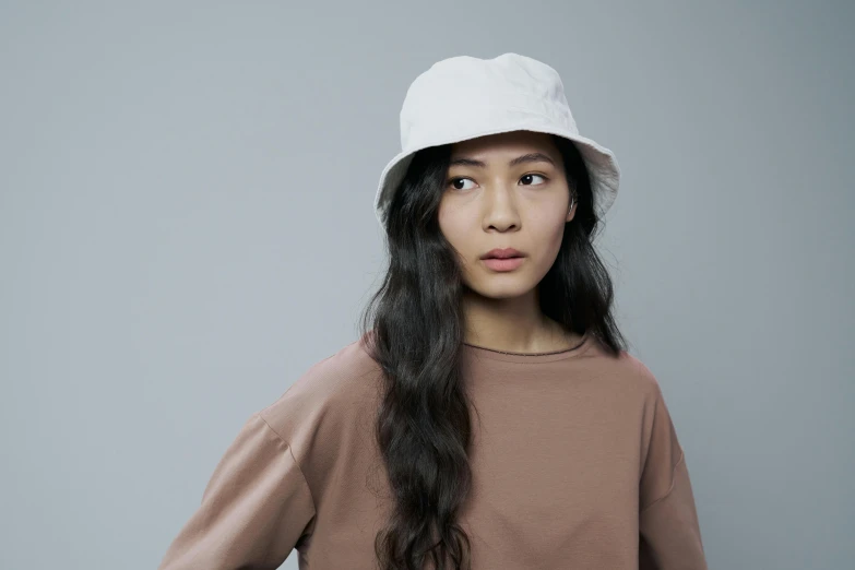 a woman in a brown shirt and a white hat, inspired by Kim Tschang Yeul, unsplash, hurufiyya, on grey background, bucket hat, pale-skinned persian girl, full product shot