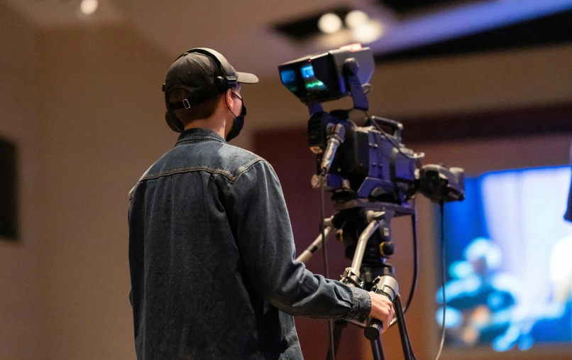 a man standing in front of a video camera, by Everett Warner, pexels, tv program, panels, theatre equipment, facing away from camera