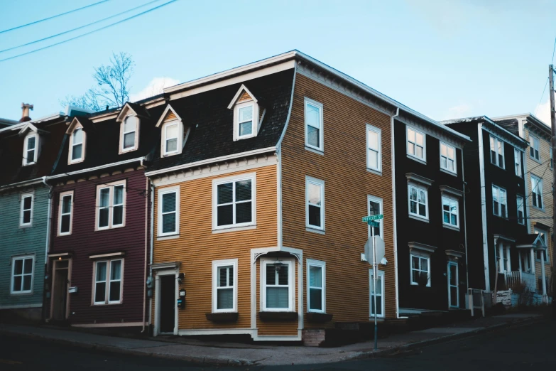 a row of multi - colored houses on a street corner, pexels contest winner, muted brown yellow and blacks, quebec, in front of a two story house, multiple wide angles