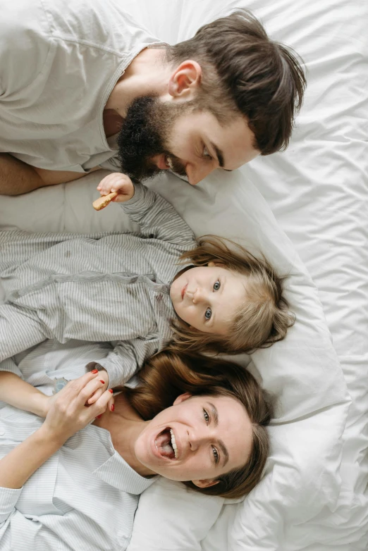 a group of people laying on top of a bed, husband wife and son, smaller mouth, sympathetic, for kids