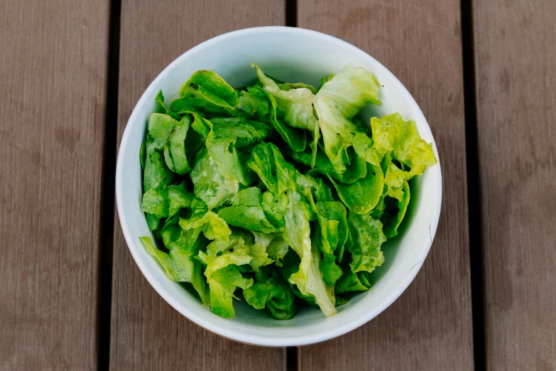 a white bowl filled with lettuce on top of a wooden table, by Kristin Nelson, pexels, 🐿🍸🍋