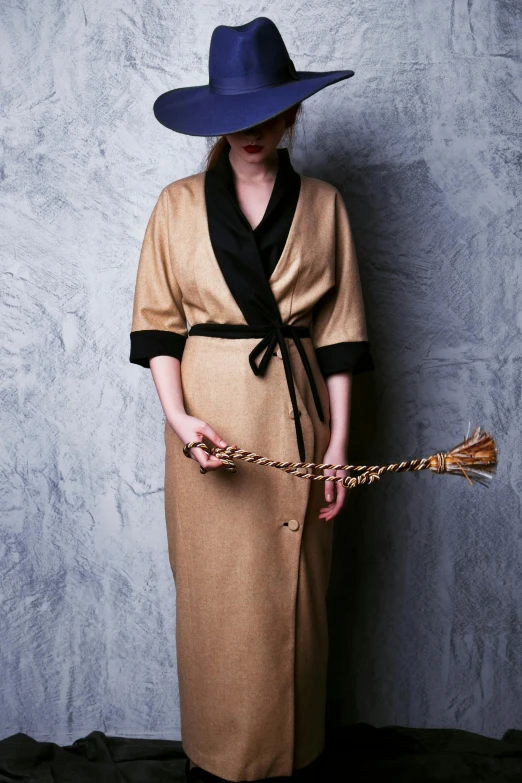 a woman in a dress and hat holding a broom, a portrait, inspired by De Hirsh Margules, dirty linen robes, award winning fashion photo, light brown trenchcoat, 1 9 5 0 s style