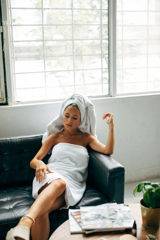 a woman sitting on a couch with a towel on her head, trending on unsplash, wearing a wet white short dress, smoking woman, clean hair, skincare