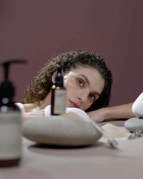 a woman laying on top of a bed next to a bottle of liquid, trending on pexels, mannerism, spa, sitting on a lab table, full face, product introduction photo